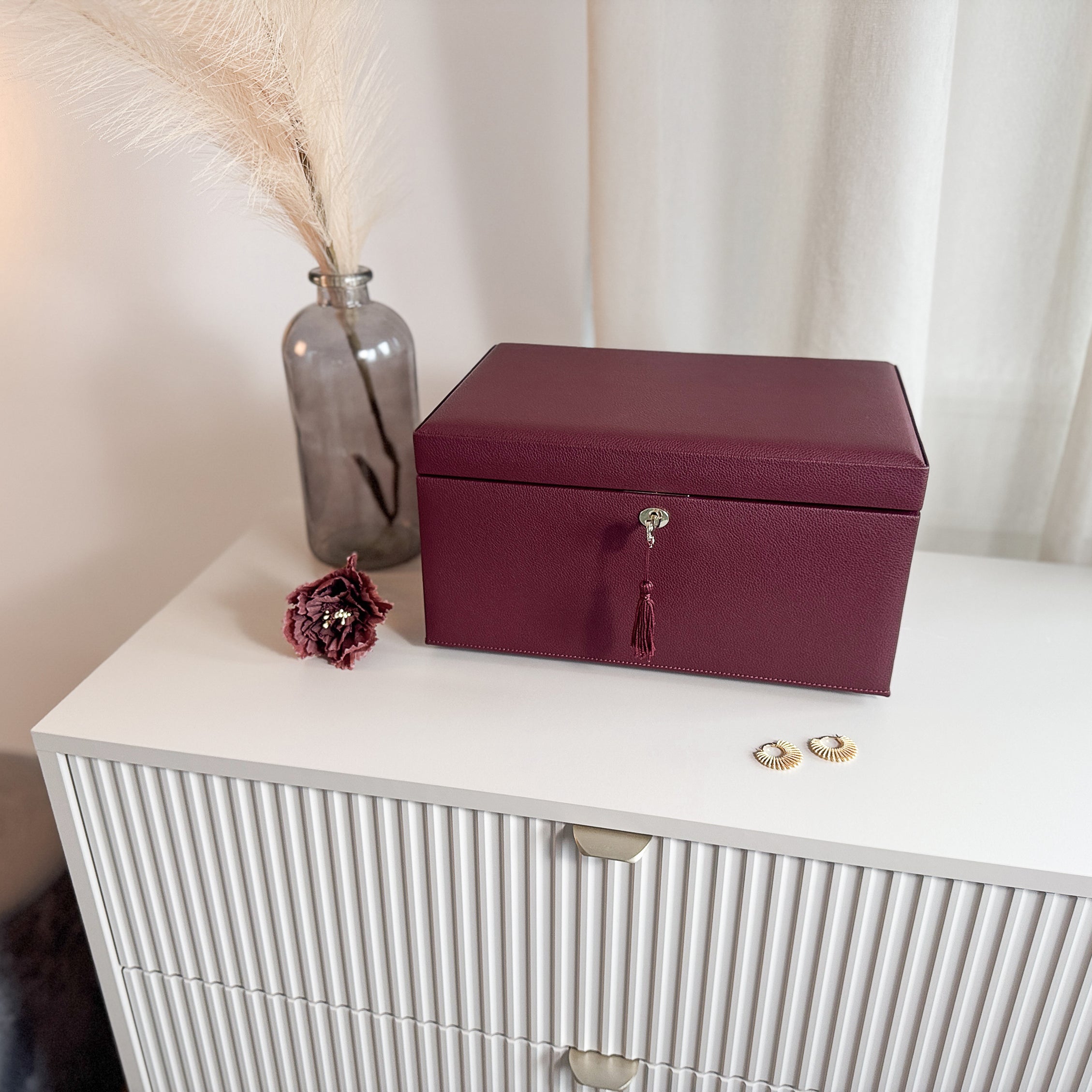 Grande boîte à bijoux en cuir bordeaux de la collection Vitoria. Vue fermée, posée sur une commode