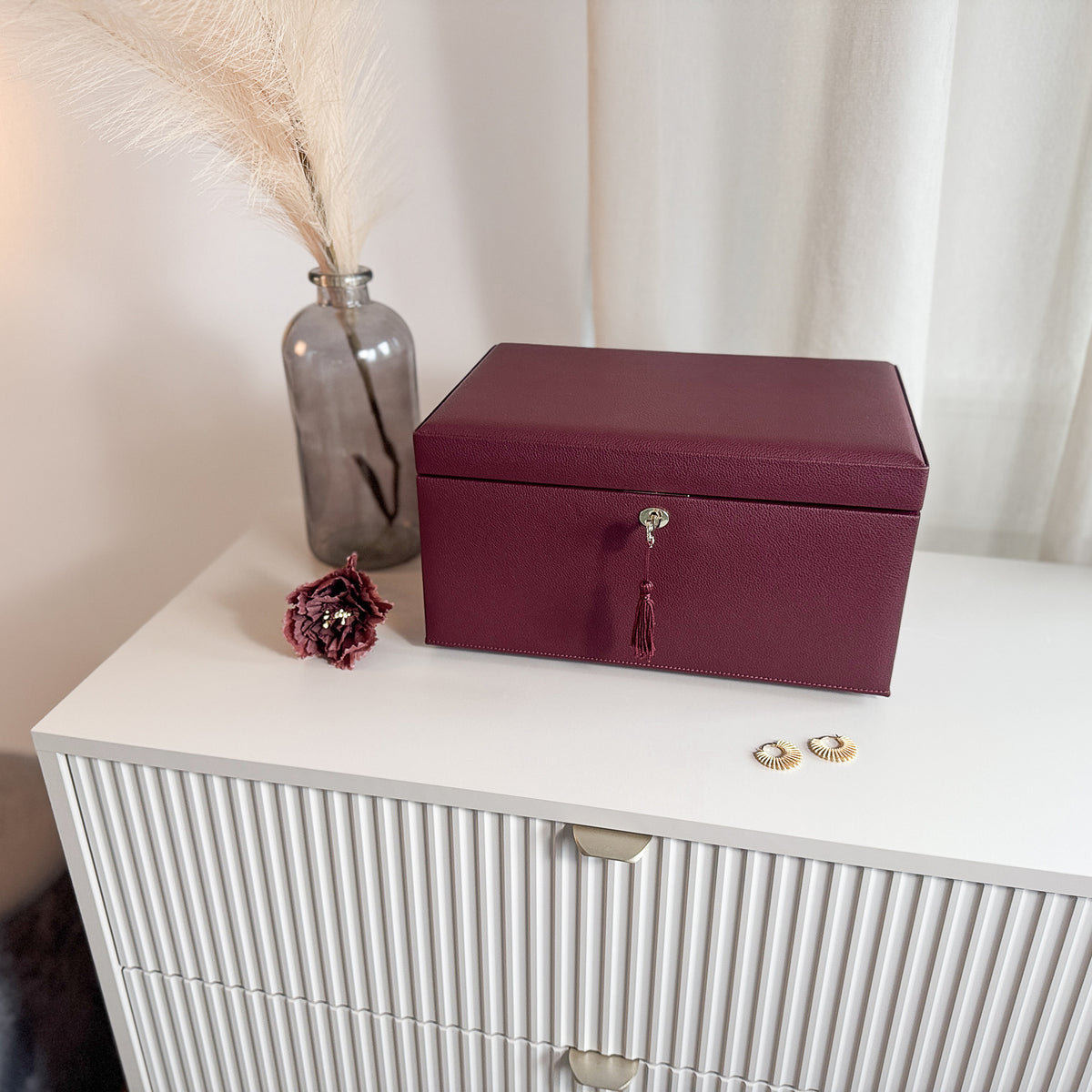 Grande boîte à bijoux en cuir bordeaux de la collection Vitoria. Vue fermée, posée sur une commode