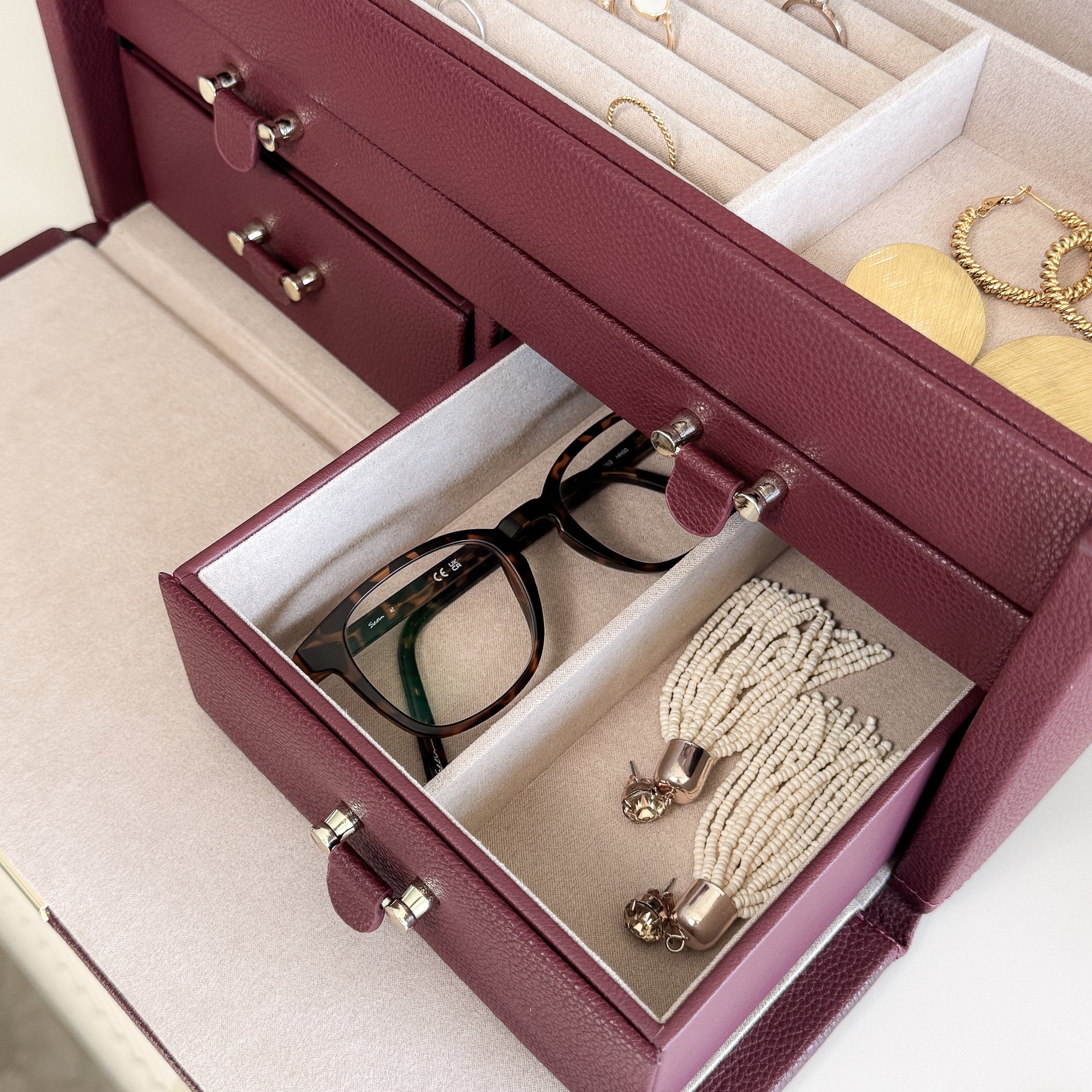 Grande boîte à bijoux en cuir bordeaux de la collection Vitoria. Vue ouverte, remplie de bijoux et d'une paire de lunette