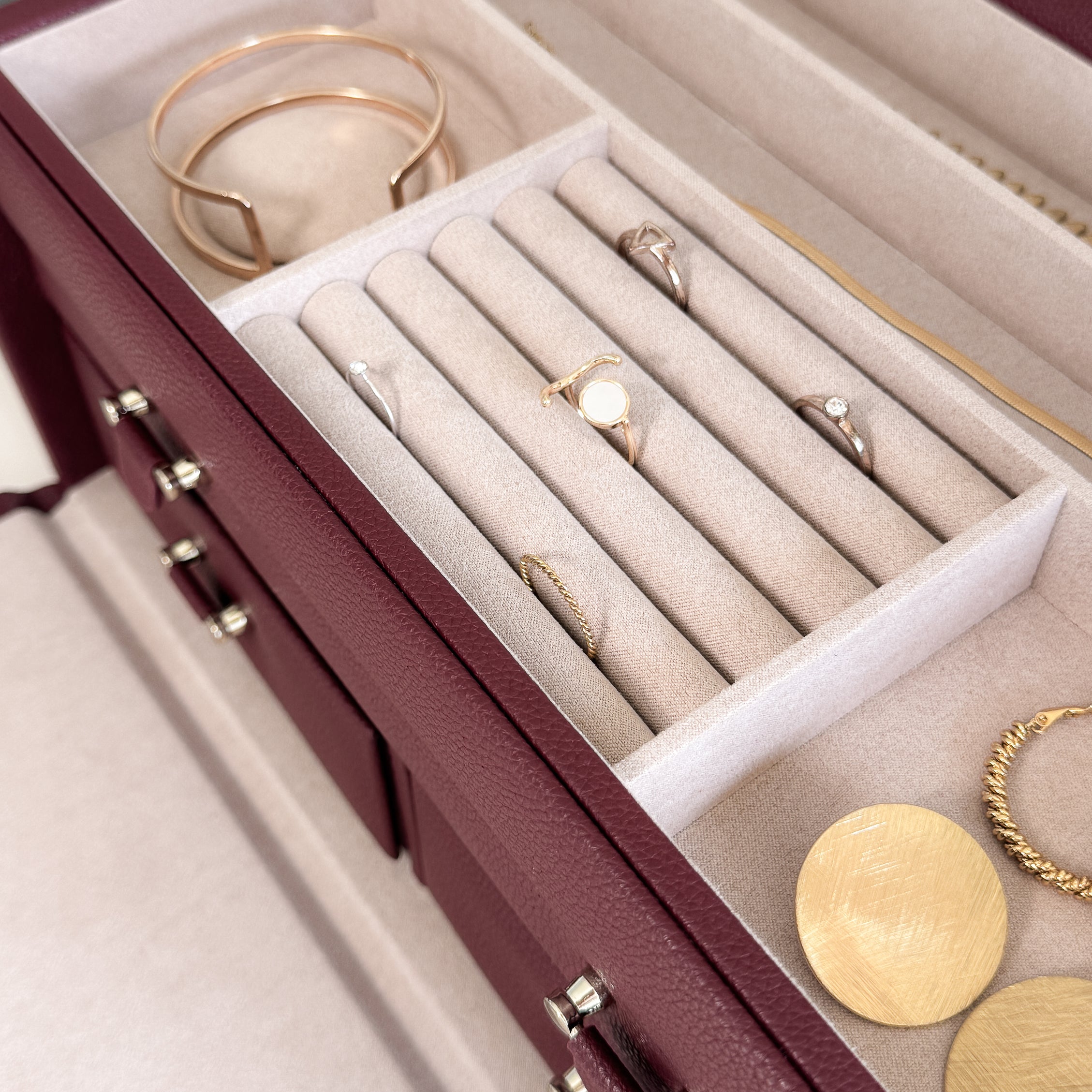 Grande boîte à bijoux en cuir bordeaux de la collection Vitoria. Vue ouverte, remplie de bijoux avec un zoom sur le compartiments à bagues