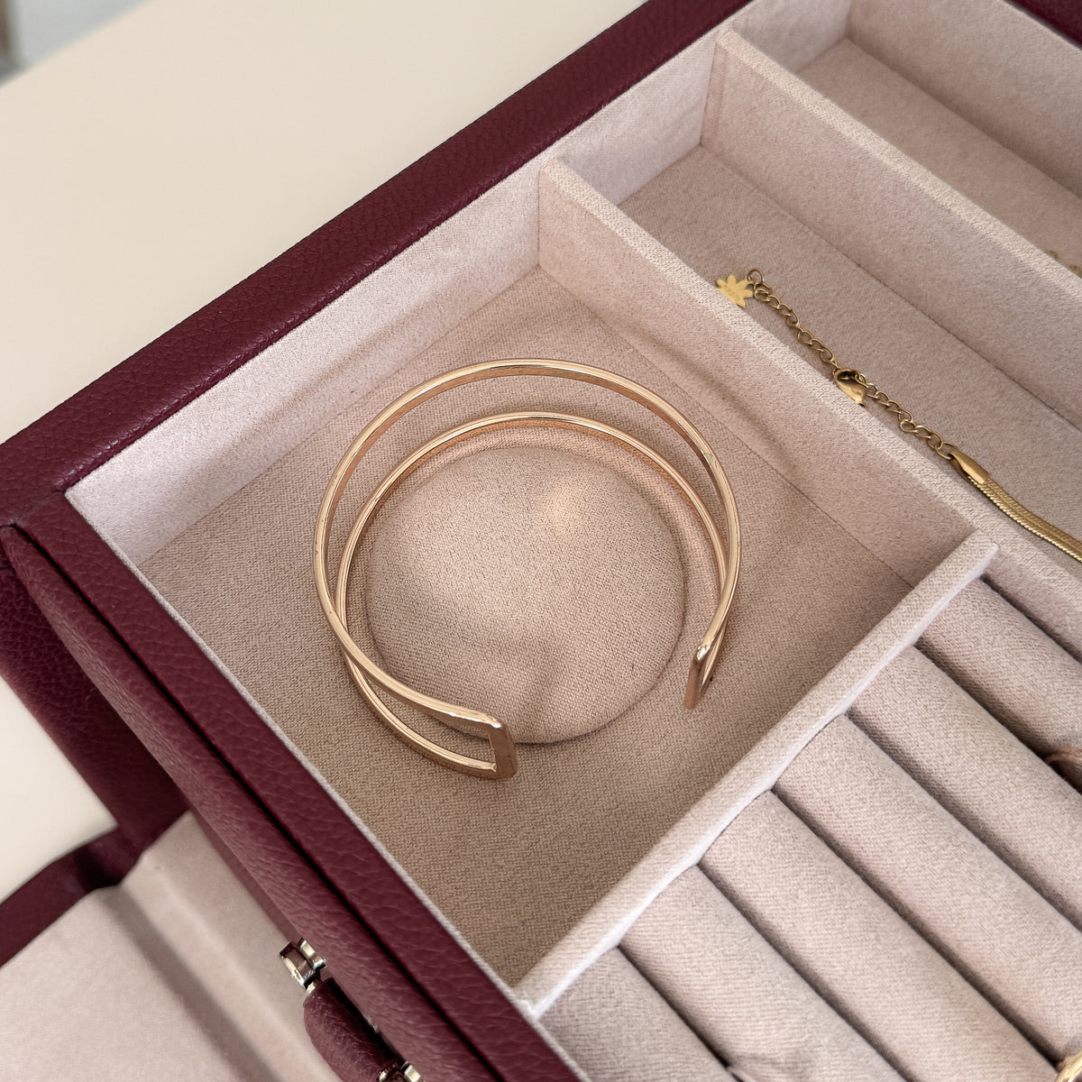 Grande boîte à bijoux en cuir bordeaux de la collection Vitoria. Vue ouverte, remplie de bijoux avec un zoom sur un bracelet de type jonc