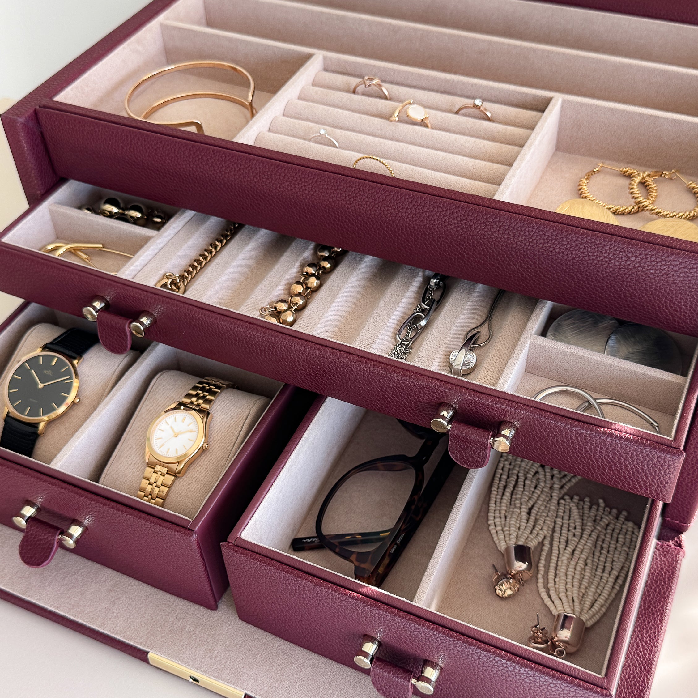 Grande boîte à bijoux en cuir bordeaux de la collection Vitoria. Vue ouverte, remplie de bijoux avec un zoom sur les tiroirs à bijoux