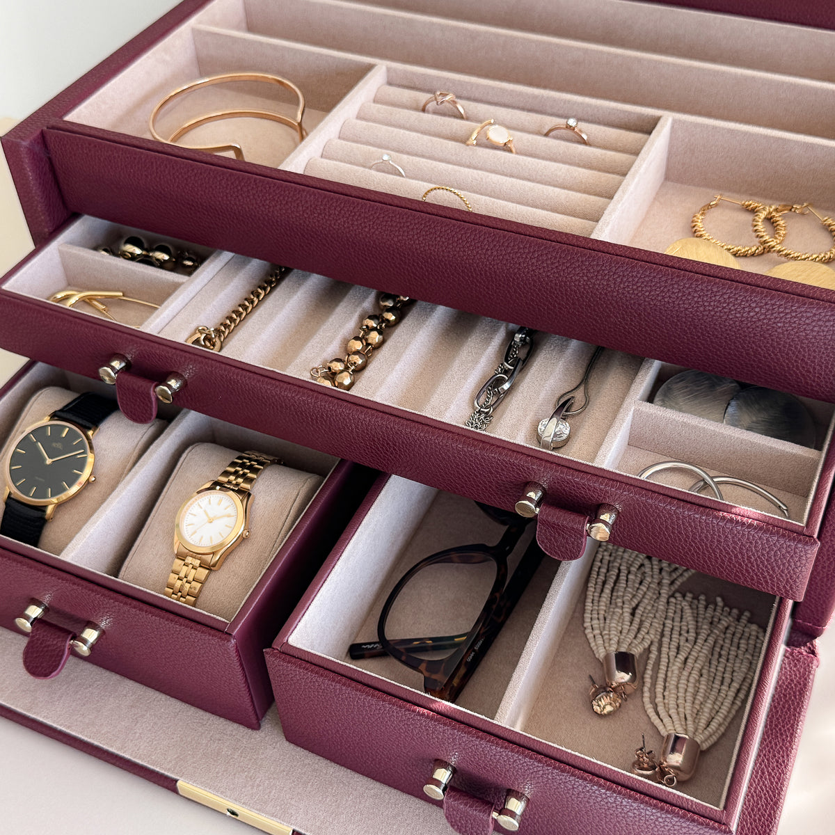 Grande boîte à bijoux en cuir bordeaux de la collection Vitoria. Vue ouverte, remplie de bijoux avec un zoom sur les tiroirs à bijoux