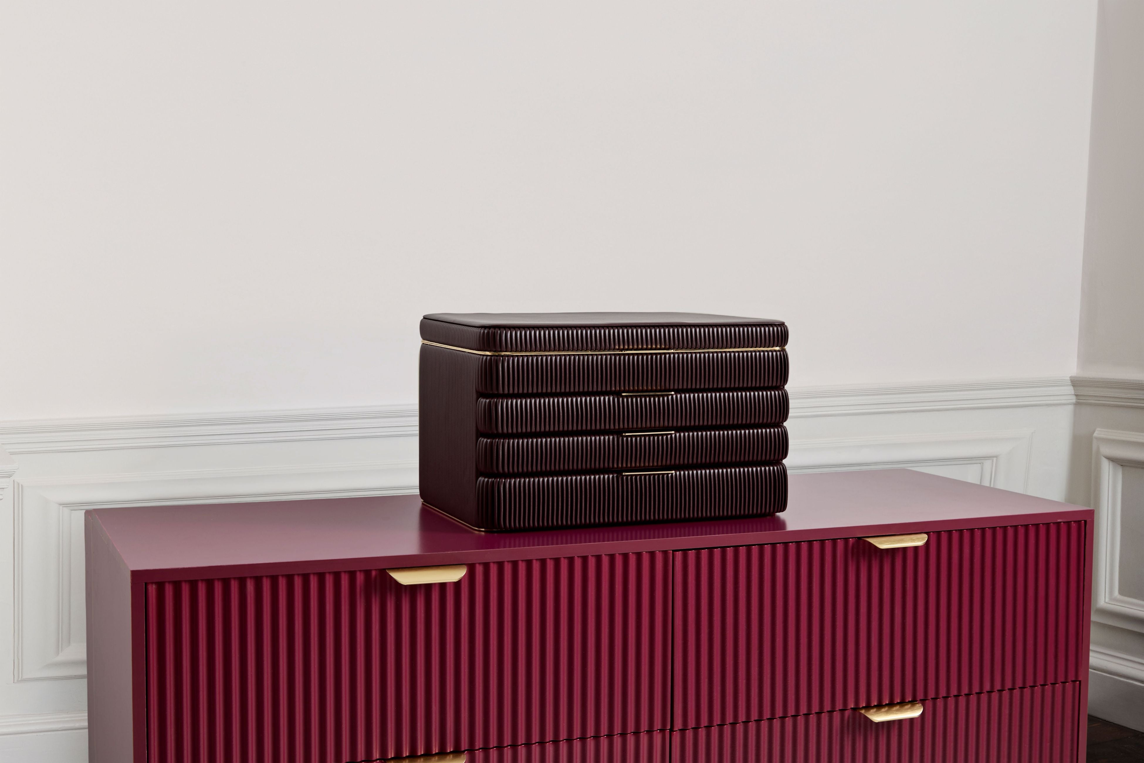 Armoire à bijoux couleur bordeaux de la collection Bella de la manufacture Wolf 1834. Vue de transverse fermée, posée sur une commode ton sur ton.