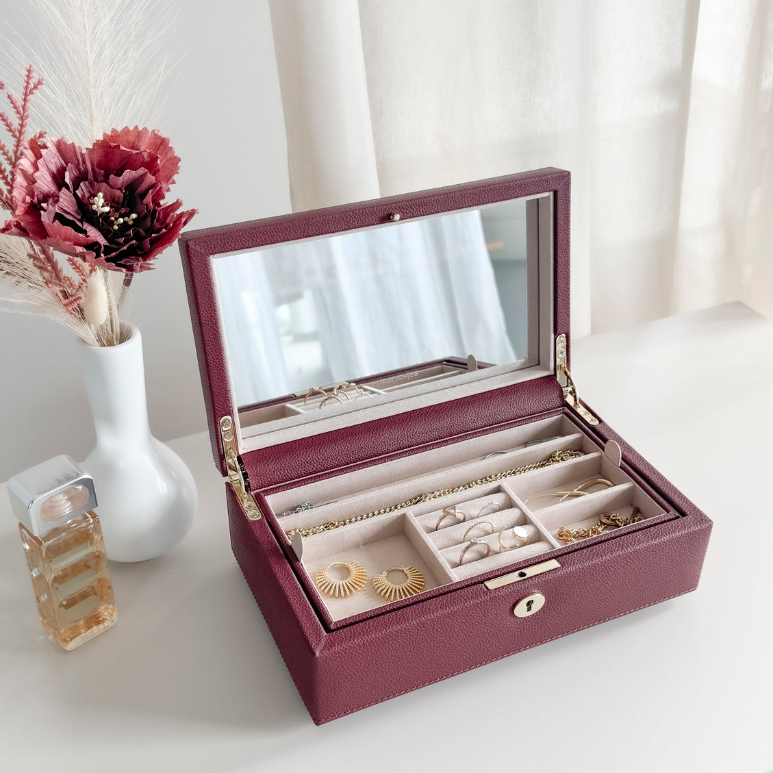 Boîte à bijoux en cuir bordeaux de la collection Vitoria. Vue ouverte et remplie de bijoux, posée sur une commode