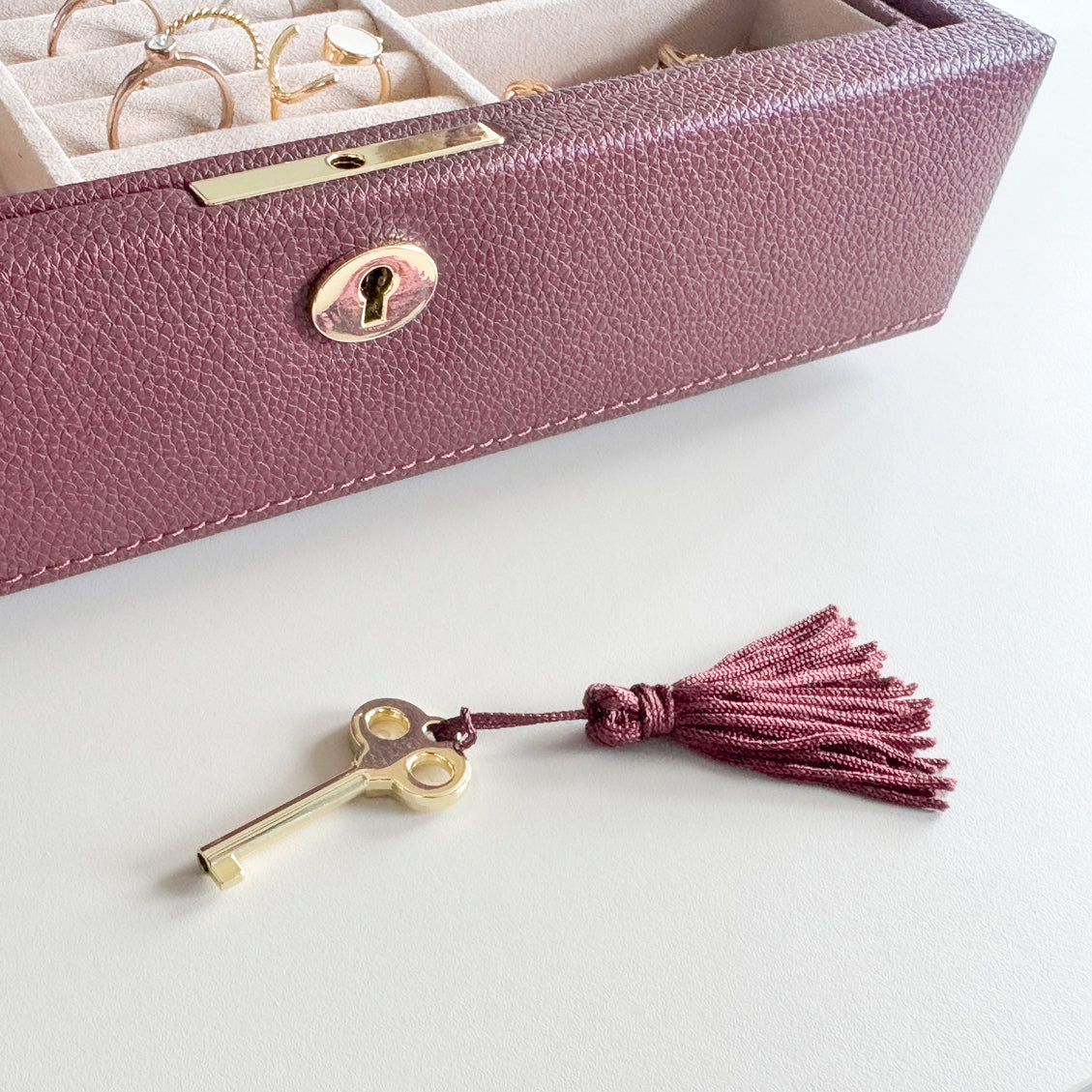 Boîte à bijoux en cuir bordeaux de la collection Vitoria. La boîte est posée sur une commode, et il y a un zoom sur la serrure et la clé dorée