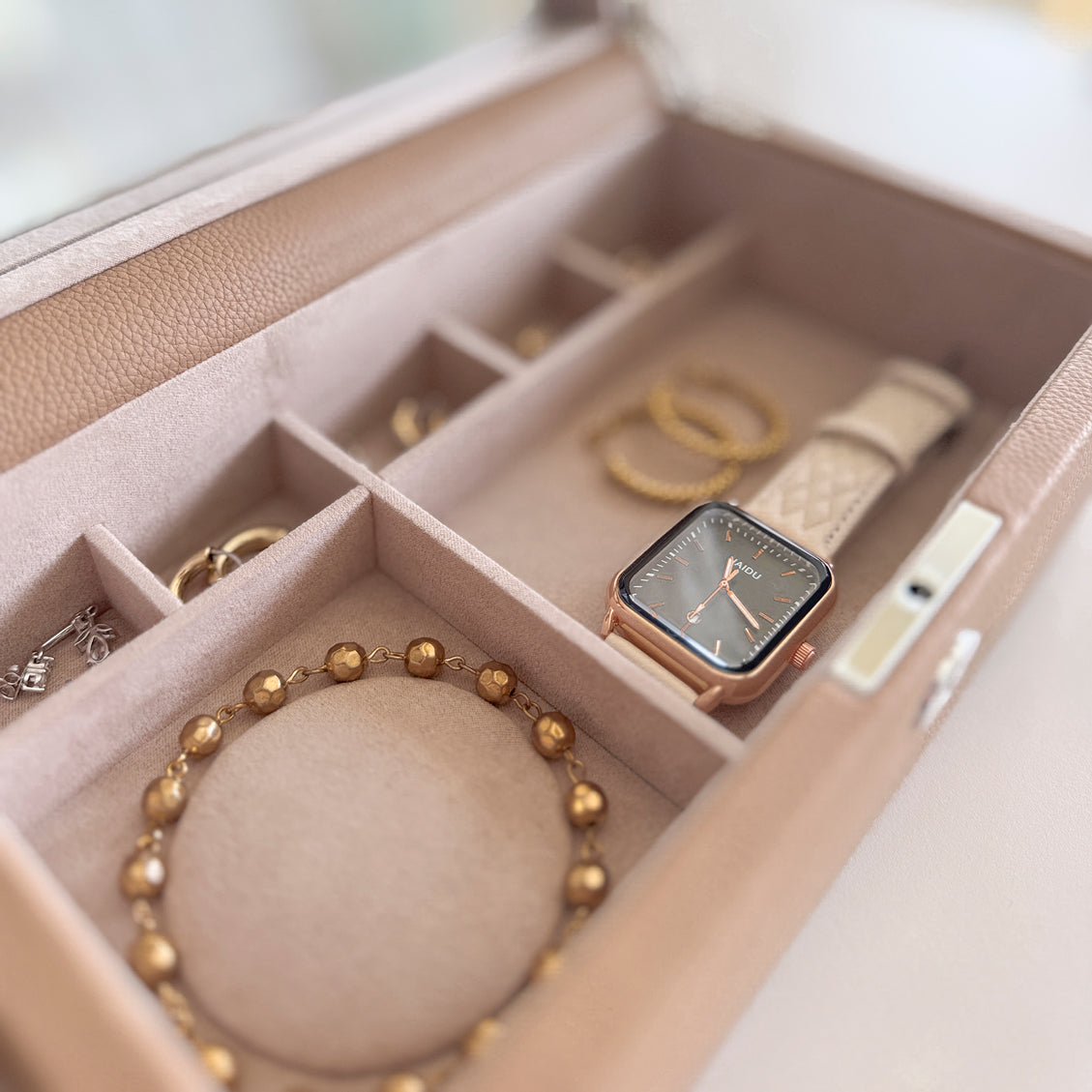 Boîte à bijoux en cuir cappuccino de la collection Vitoria. Vue ouverte, zoom sur les compartiments intérieurs remplis de bijoux et montres
