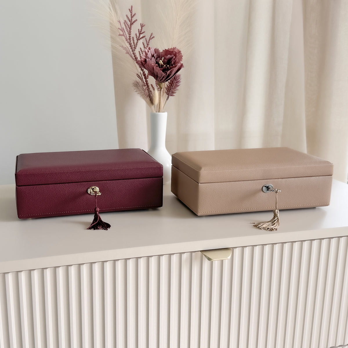 Vue côte à côte fermée des boîtes à bijoux en cuir cappuccino et bordeaux de la collection Vitoria. Posées sur une commode