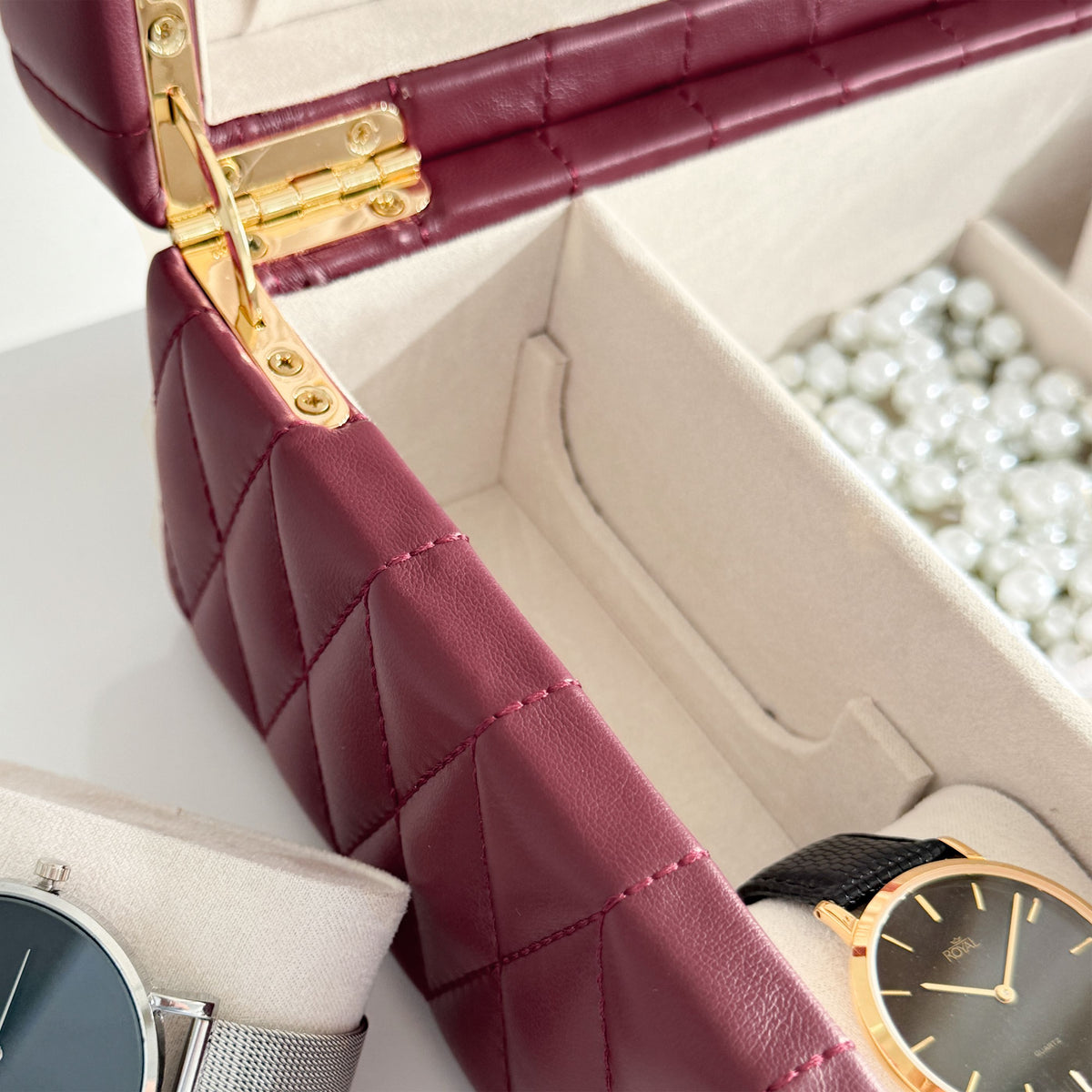 Boîte à bijoux matelassé Saphira bordeaux. Zoom sur les compartiments intérieurs remplis de bijoux et montres