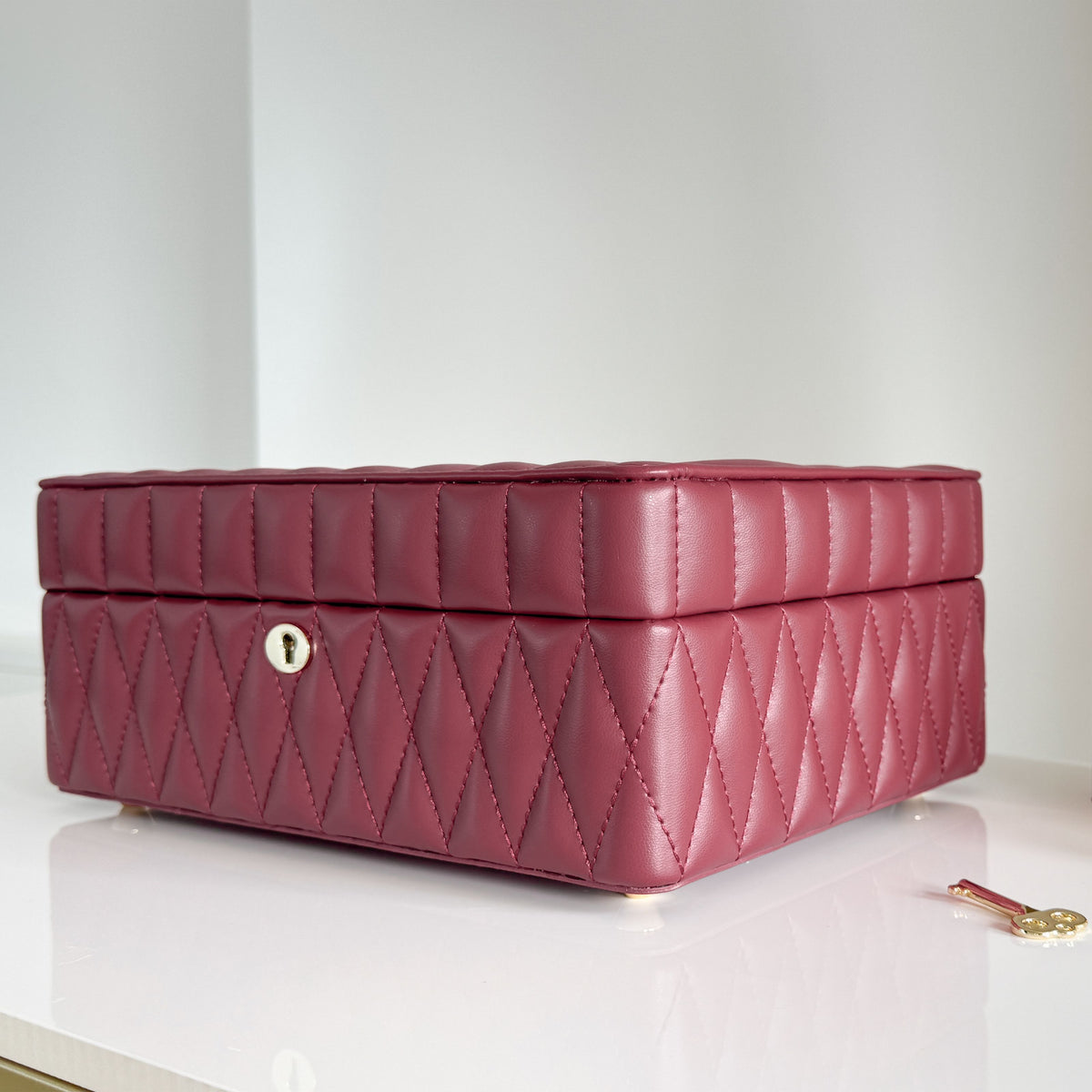 Boîte à bijoux matelassé Saphira bordeaux. Vue de transverse face de la boîte à bijoux posée sur une commande blanche brillante