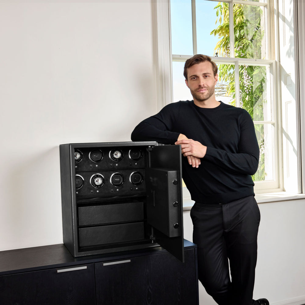 Coffre fort biométrique et remontoir vertemplacements de la collection The Den, manufacture Wolf 1834, coloris noir.
Le coffre fort est posé sur une commode noir et un homme est debout sur la gauche du coffre, accoudé dessus, les mains l'une sur l'autre