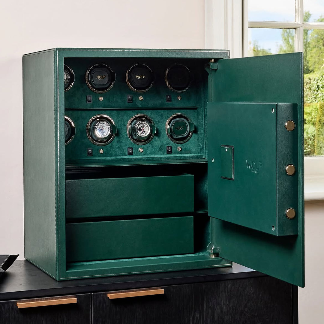 Coffre fort biométrique et remontoir vertemplacements de la collection The Den, manufacture Wolf 1834, coloris vert Le coffre fort est posé sur une commode noire et ouvert. Deux montres sont dans les emplacements remontoirs