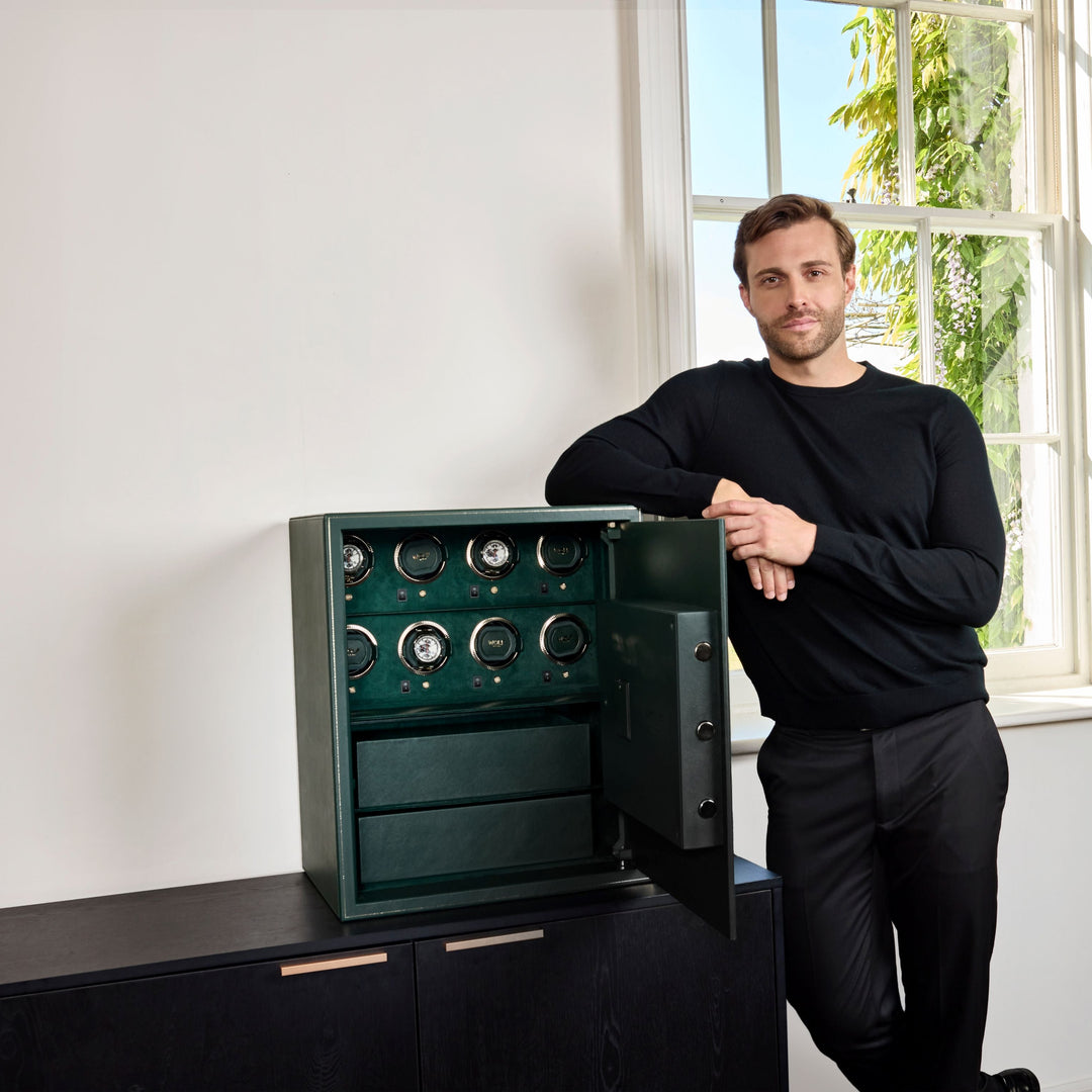 Coffre fort biométrique et remontoir vertemplacements de la collection The Den, manufacture Wolf 1834, coloris vert.
Le coffre fort est posé sur une commode noir et un homme est debout sur la gauche du coffre, accoudé dessus, les mains l'une sur l'autre