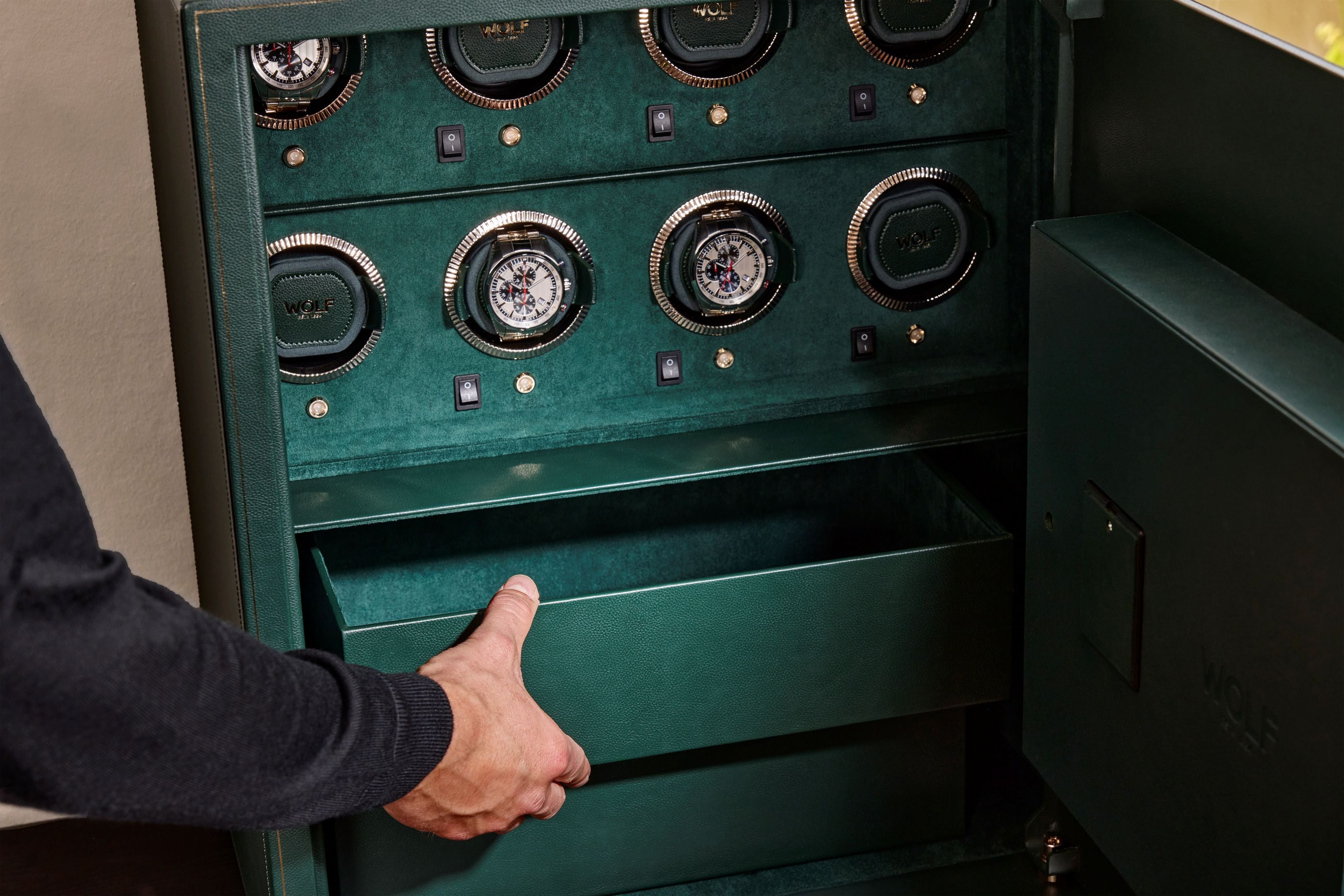 Coffre fort biométrique et remontoir vertemplacements de la collection The Den, manufacture Wolf 1834, coloris vert.
Le coffre fort est ouvert et une main d'homme se saisit d'un des coffrets de rangement du coffre