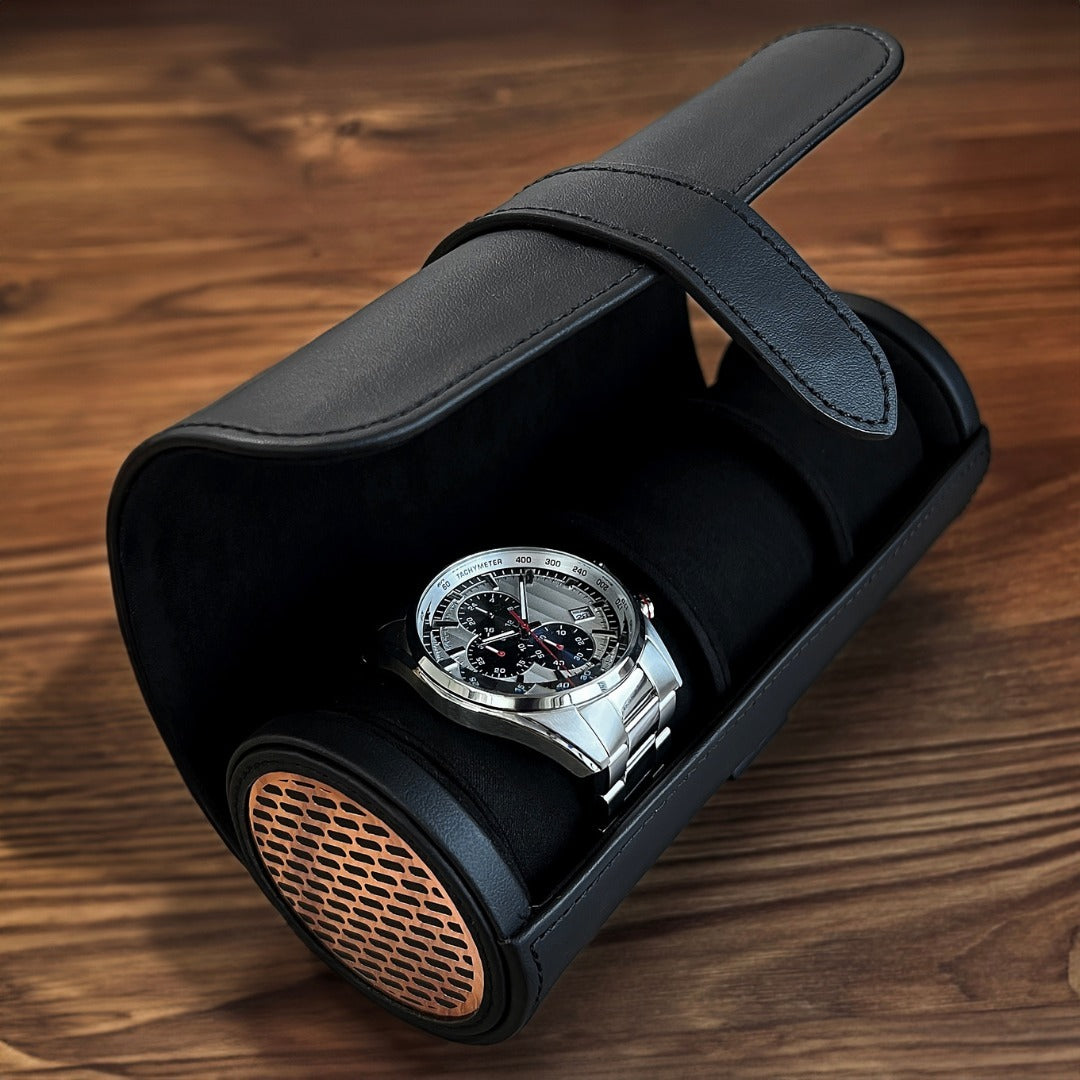 Étui pour montre en cuir noir avec grille cuivrée, contenant une montre en métal posée sur coussin