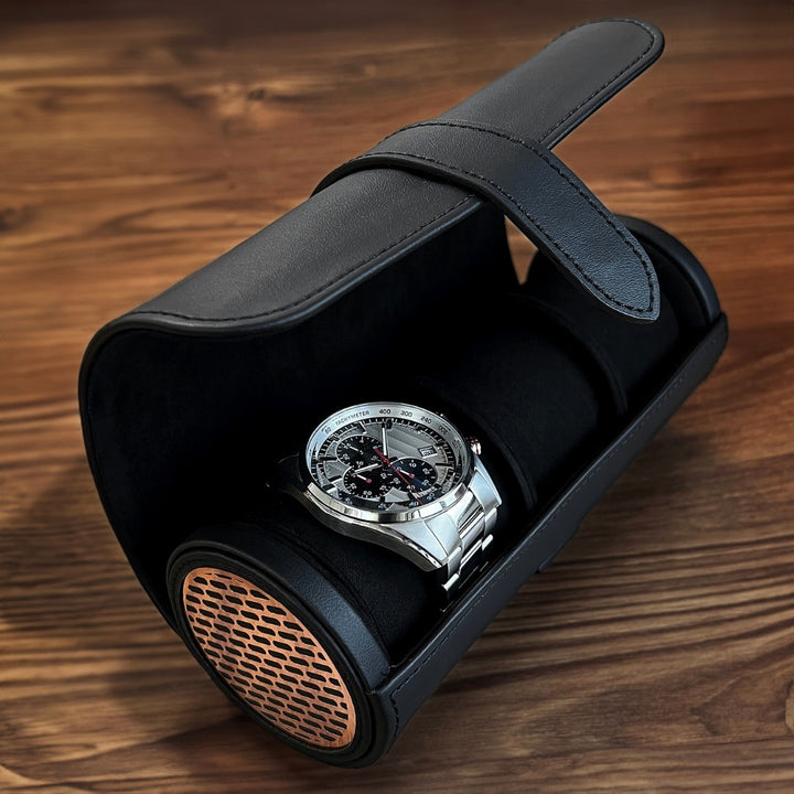 Étui pour montre en cuir noir avec grille cuivrée, contenant une montre en métal posée sur coussin
