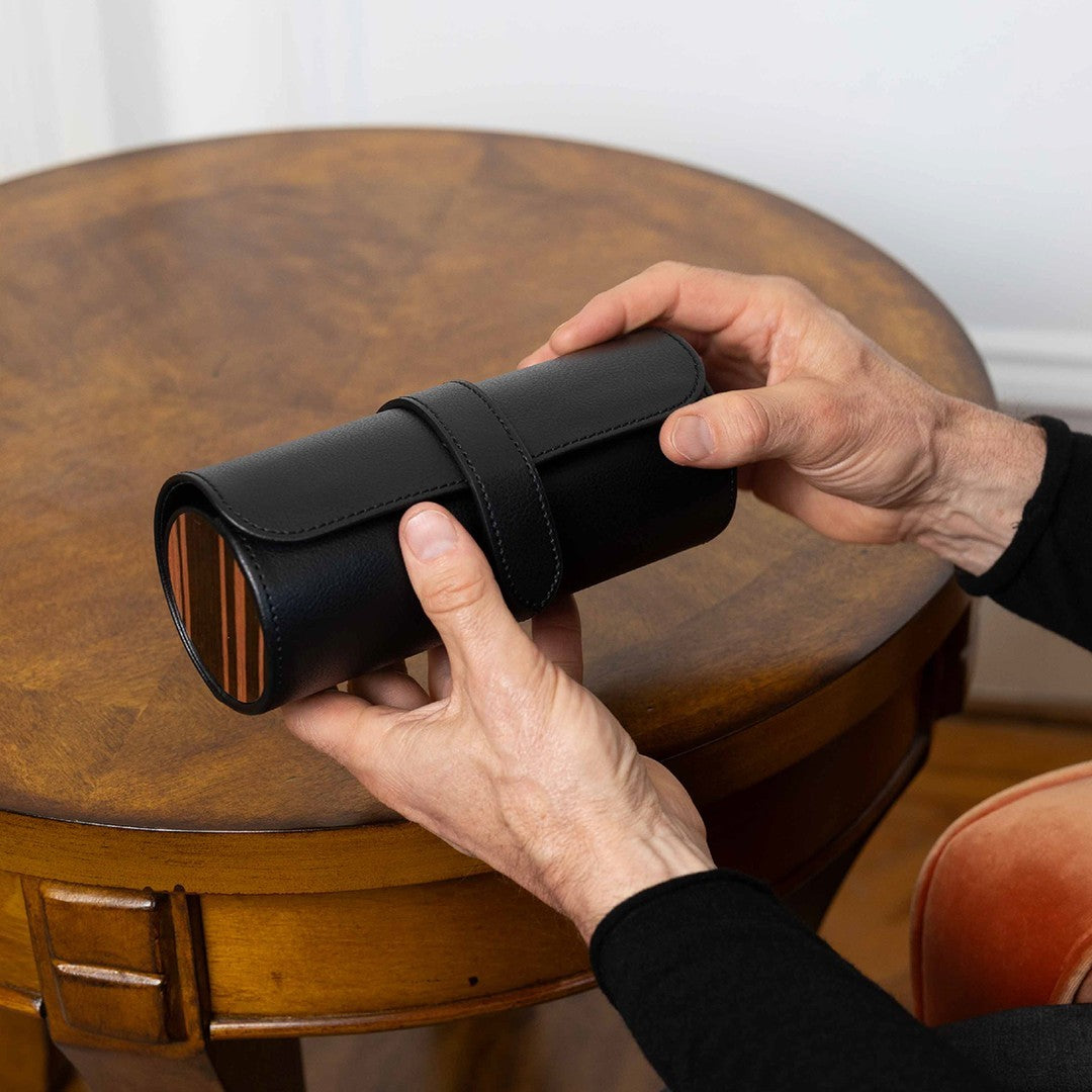 Un homme tient un étui de voyage cylindrique noir pour montre, fermé et doté de côtés décorés façon bois