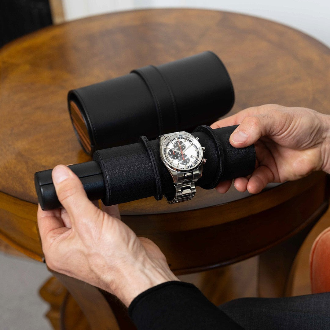 Un homme retire une montre de son étui de voyage cylindrique noir, en tenant le support rembourré avec les deux mains