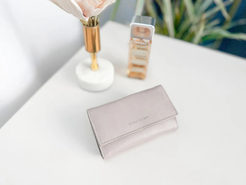 Pochette en cuir véritable Sienna, cuir véritable, beige cappuccino fermé sur une table, à côté d'autres accessoires