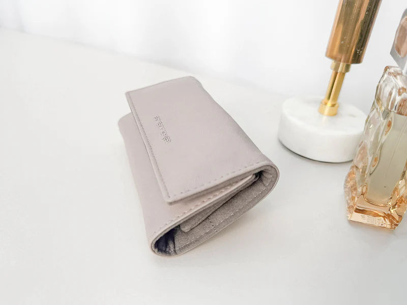 Pochette en cuir véritable Sienna, cuir véritable, beige cappuccino fermé sur une table, à côté d'autres accessoires