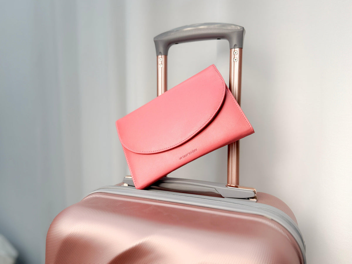 Grand étui à bijoux de voyage en cuir véritable Sienna, rose corail, vue fermé, de face, posé sur une valise de couleur rose irisé