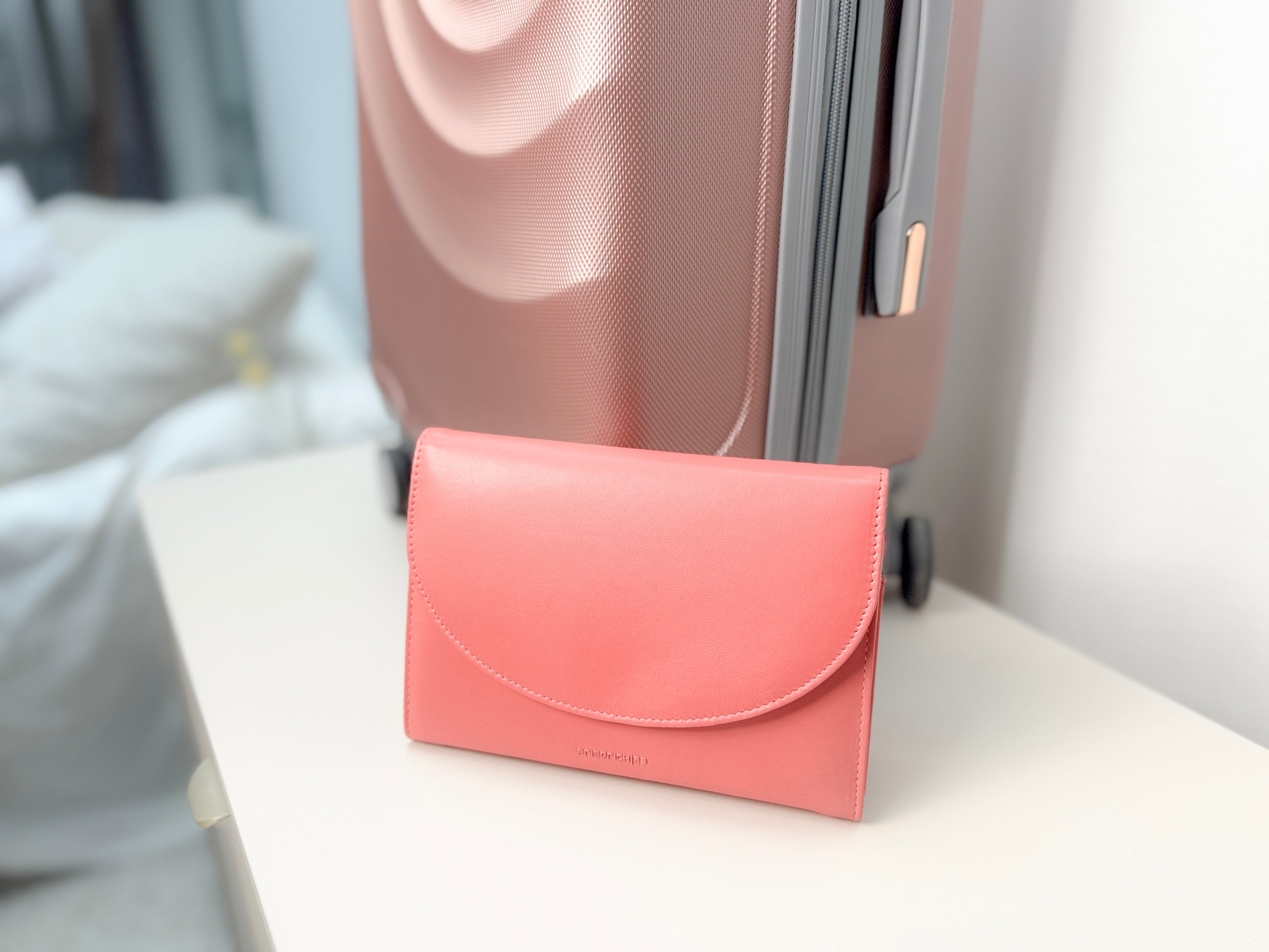 Grand étui à bijoux de voyage en cuir véritable Sienna, rose corail, vue fermée contre une valise rose irisé