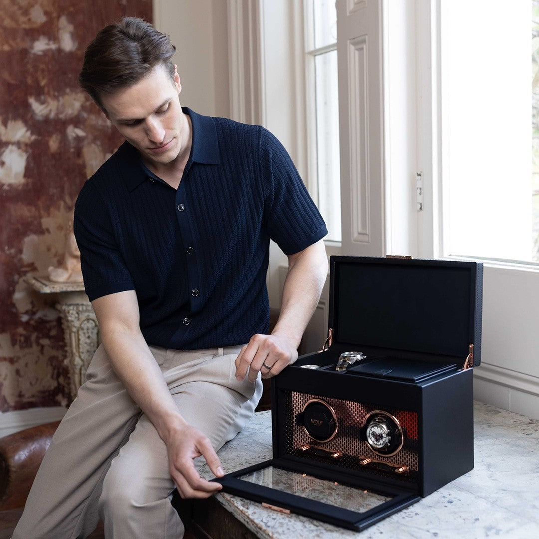 Un homme ouvre une  remontoir à montres Wolf  , posée sur une table près d’une fenêtre