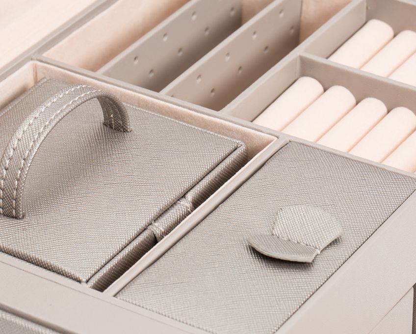 Intérieur d’une boite à bijoux grise avec plusieurs compartiments, coussinets pour bagues et petits rangements