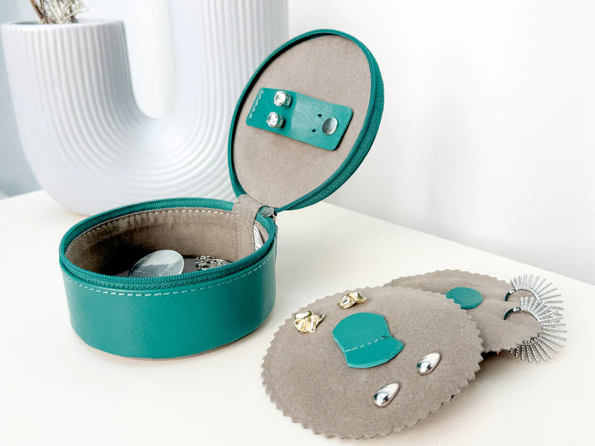 Mini boite à bijoux ronde en cuir véritable Sienna, vert turquoise, vue ouverte avec des bijoux dedans, posée sur une table avec un vase blanc en fond