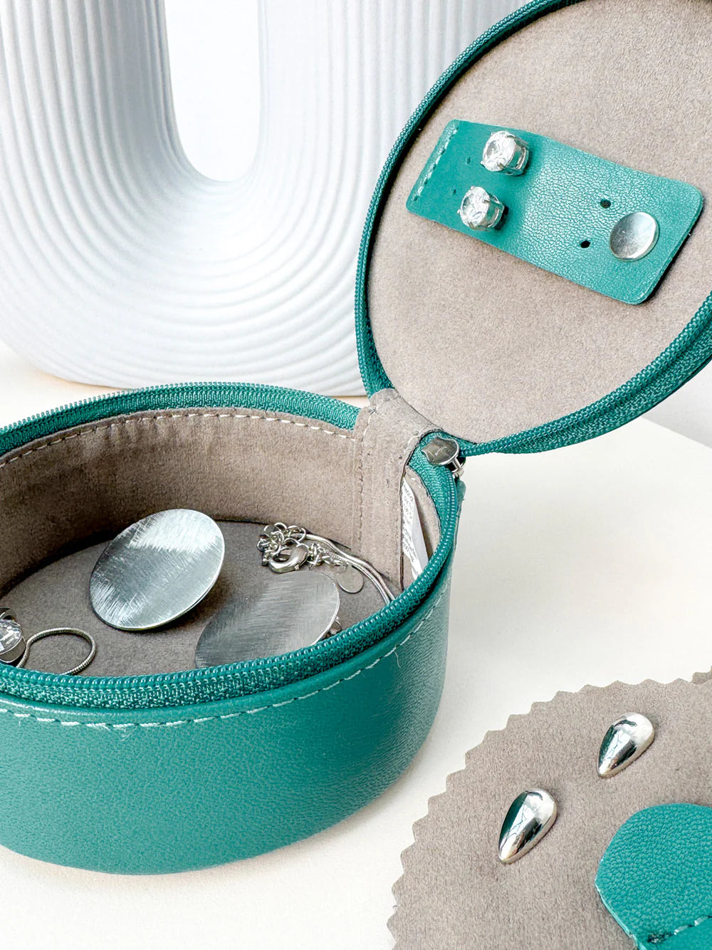 Mini boite à bijoux ronde en cuir véritable Sienna, vert turquoise, vue ouverte avec des bijoux dedans, posée sur une table avec un vase blanc en fond