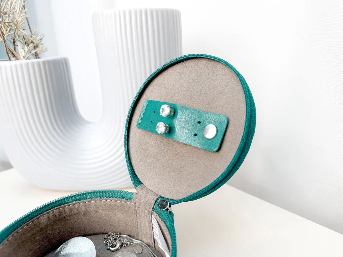 Mini boite à bijoux ronde en cuir véritable Sienna, vert turquoise, vue ouverte avec des bijoux dedans, posée sur une table avec un vase blanc en fond