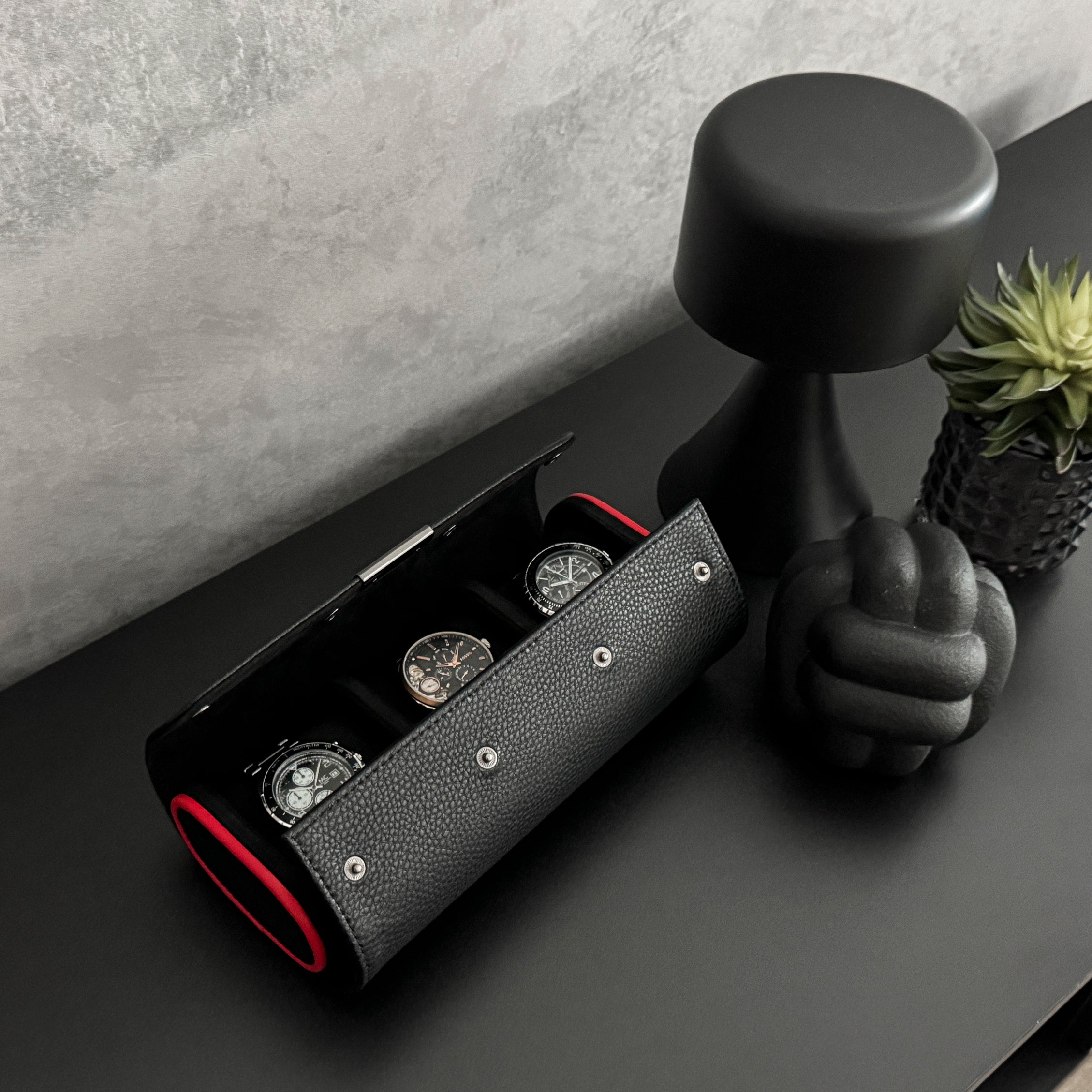 Etui à montre en cuir noir avec passepoil rouge Maranello, trois emplacements. L'étui à montre est rempli de montres, posé sur une commode noir, avec une vue de haut